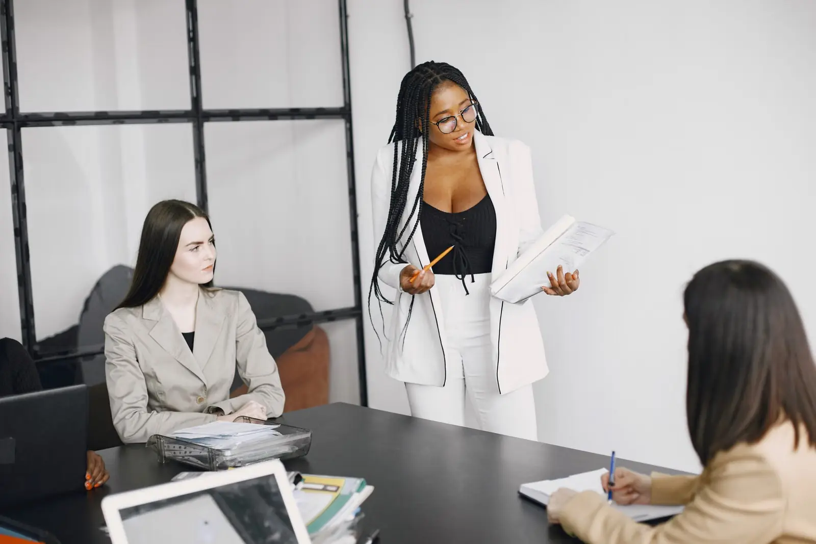 A facilitator standing at a conference table, presenting to seated colleagues who are taking notes.